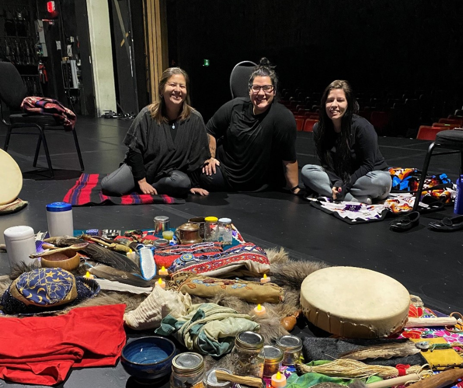 Three women on the Playhouse stage with project materials