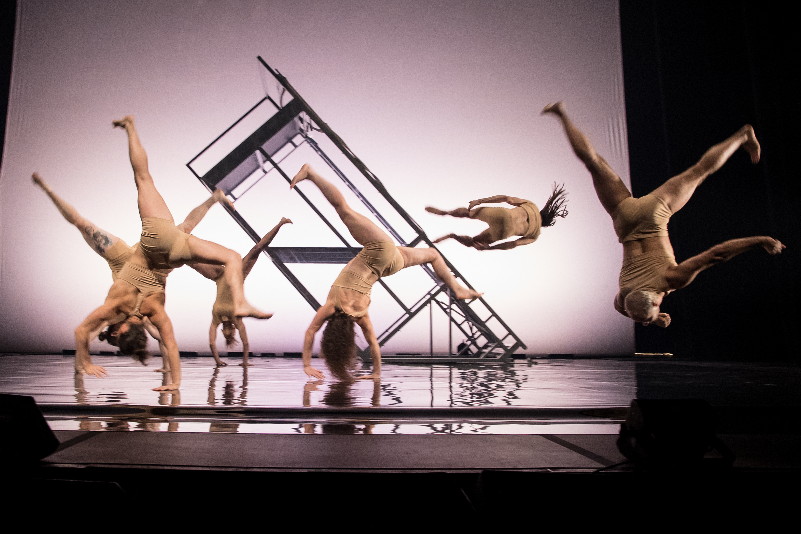 4 acrobats on stage against a light backdrop doing cartwheels and flips