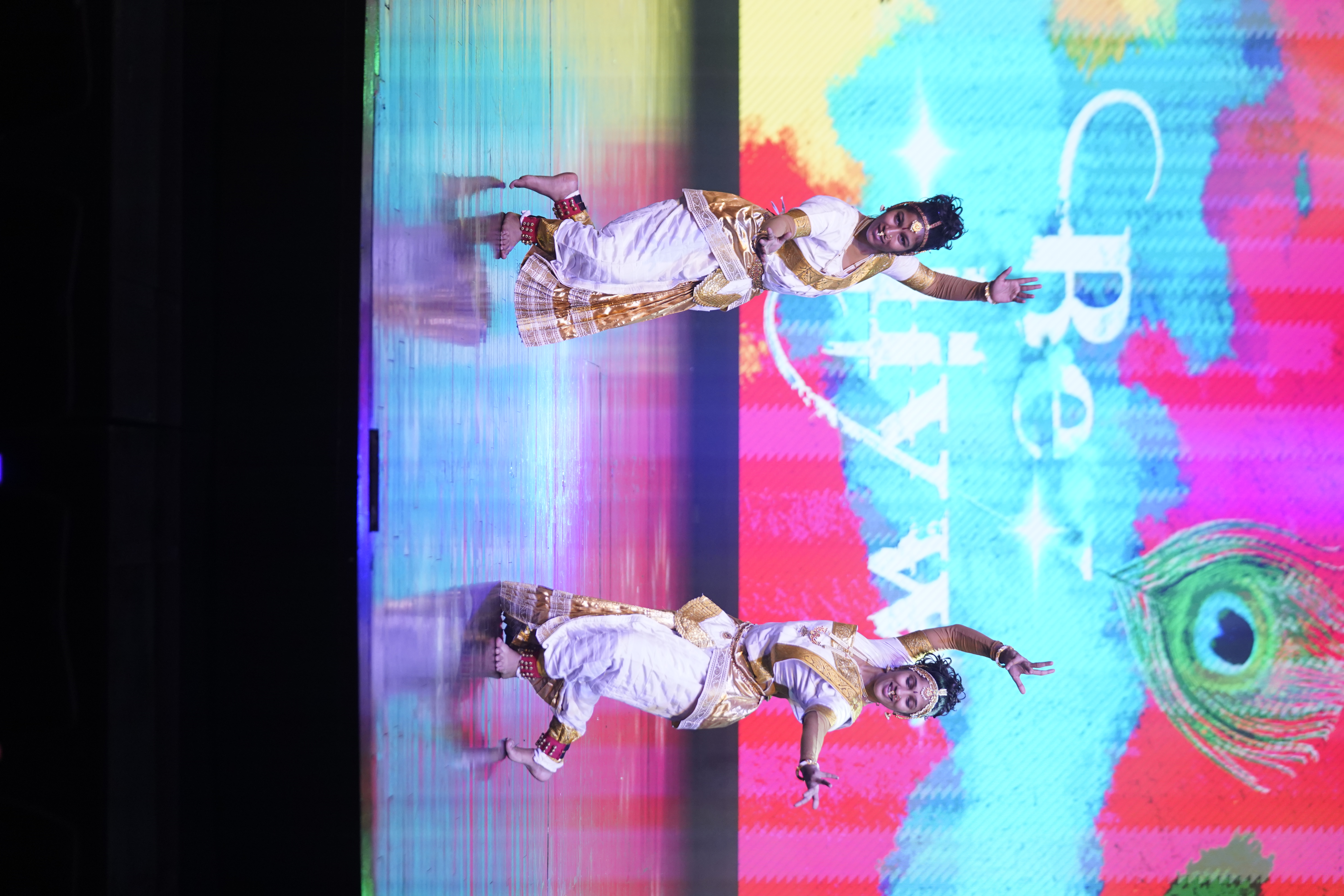 Two Indian dancers in front of a bright pink and blue background
