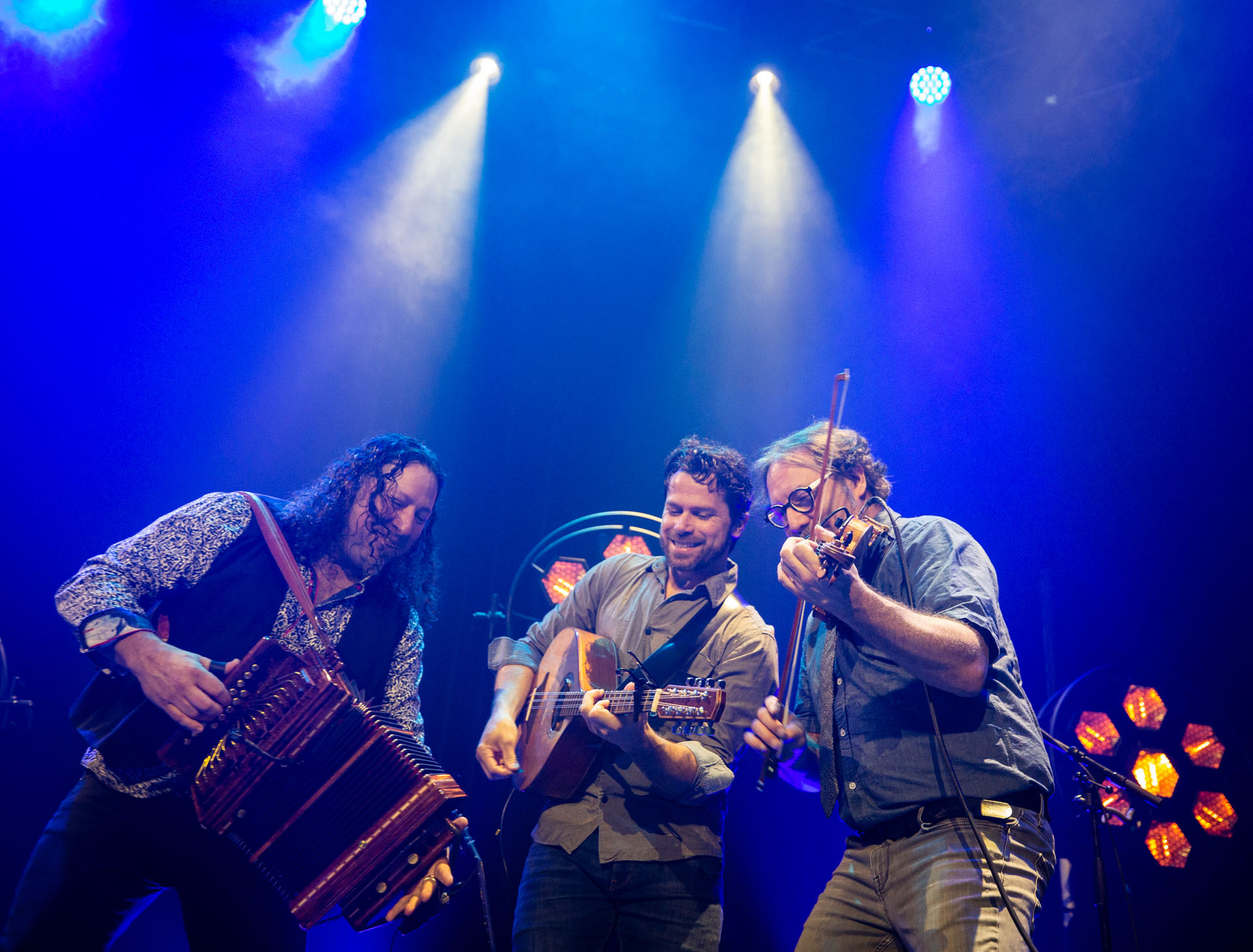 3 men playing Celtic instruments against a blue background