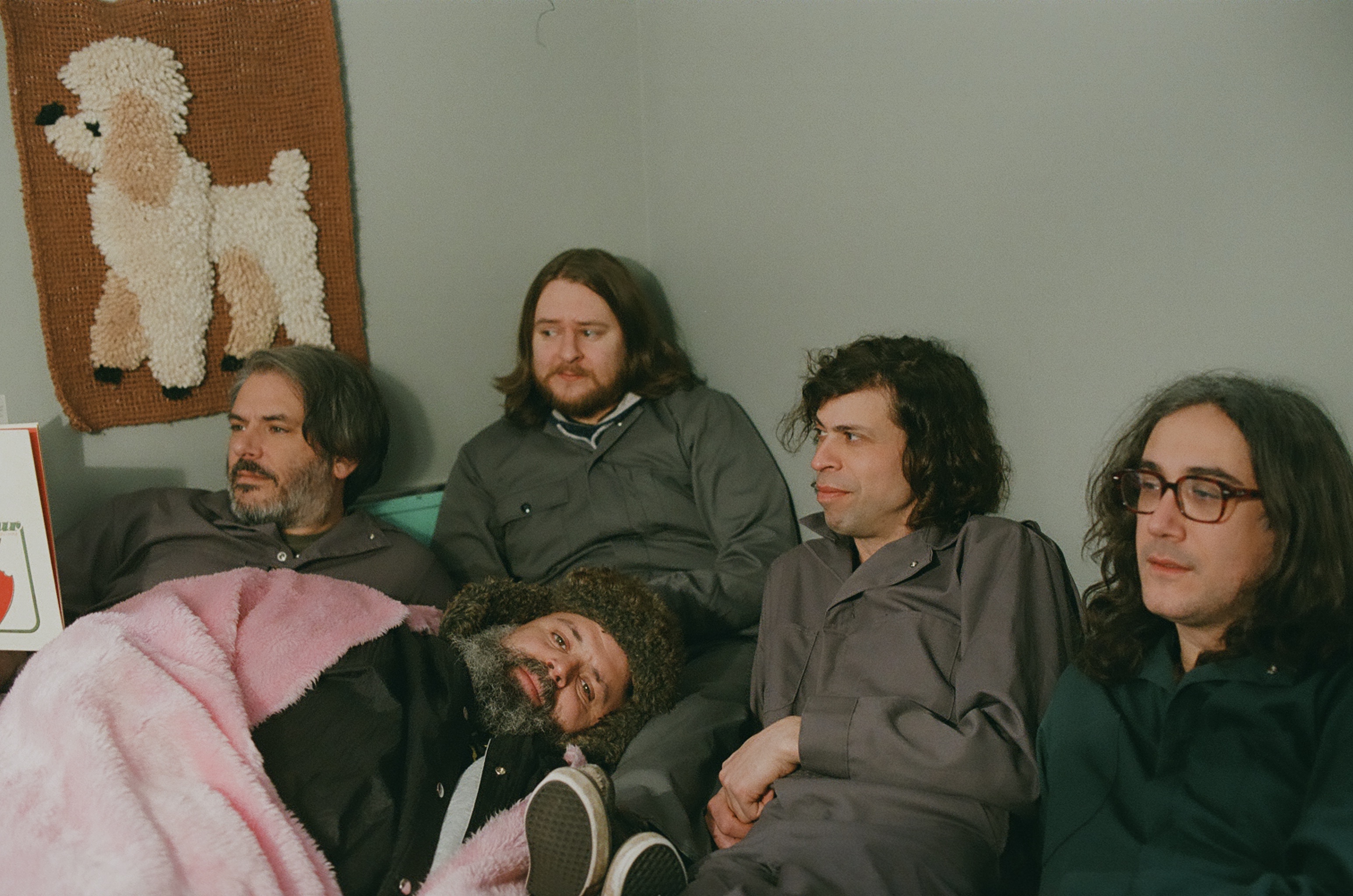 The five members of les Hôtesses d'Hilaire sitting on a couch. There is poodle artwork in the background
