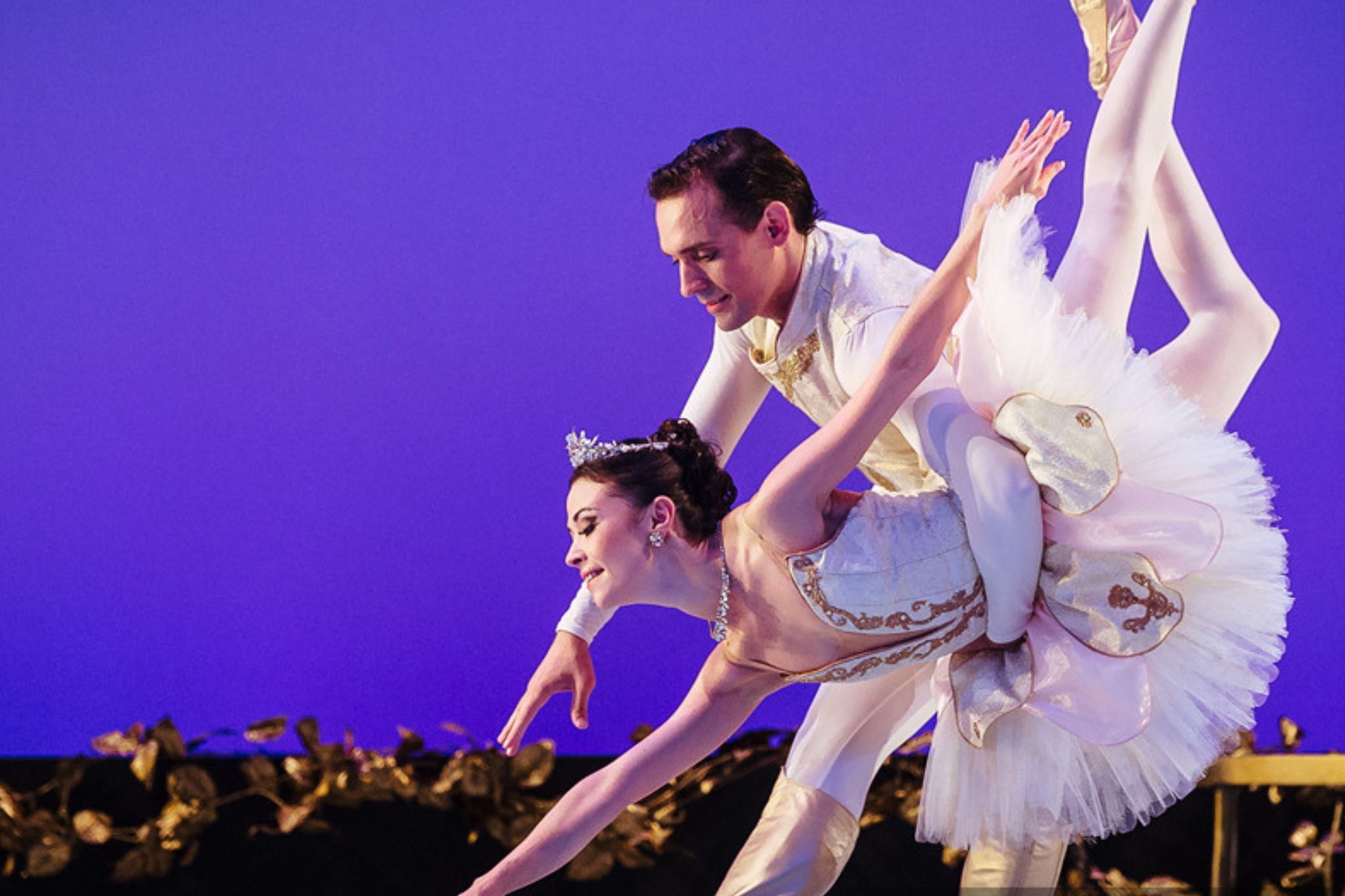 Two dancers wearing white, elegant outfits strike a graceful pose.