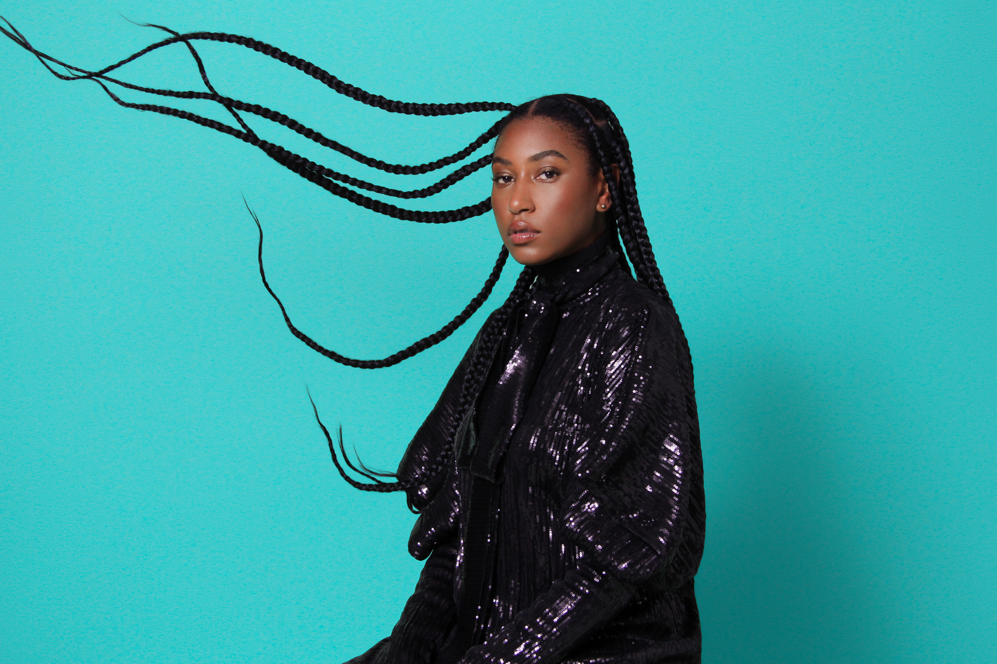 Dominique stands in front of a bright blue background wearing a stylish black leather jacket, her long hair seeming to be caught in a whirl of wind.