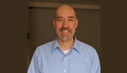 Craig Leonard wearing a light blue shirt in front of a brown background