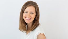 Amy Boudreau with medium length hair smiling in front of a light grey wall