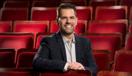 Tim Yerxa sitting against a backdrop of red theatre seats