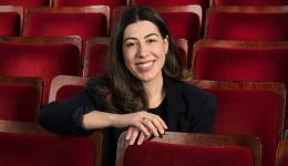 Olivia sits in the Playhouse audience, wearing black, grinning happily at the camera.