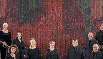 Orchestra members standing on a stairway and in a foyer dressed in black.