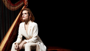 A woman sitting in a spotlight beside her harp.