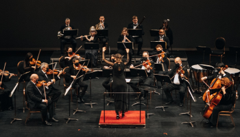 An orchestra seated on stage with their instruments.
