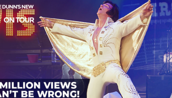 A man posing in a white and gold Elvis outfit on a stage. The word ELVIS appears to his left in large orange letters.