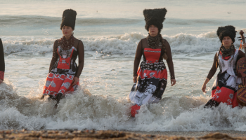4 musicians wearing black and red standing in a wave on the beach