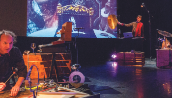 A photo of a stage filled with equipment to make different sounds and music while a film is projected in the background