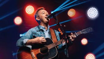 Jimmy Rankin on stage singing and playing guitar with bright lights in the background.