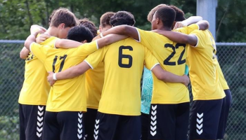 Young soccer players huddled with their arms around each other wearing their yellow jerseys. 