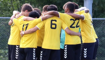 Young soccer players huddled with their arms around each other wearing their yellow jerseys.