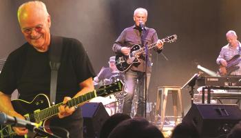 Ian Thomas, on stage with a band playing behind him.