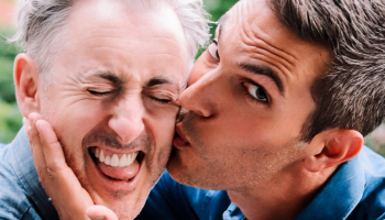 Alan Cumming making a scrunched face as Ari Shapiro kisses his cheek