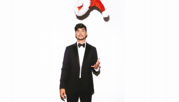 Tyler Shaw in a black suit tossing a Santa hat in the air, standing against a white background