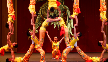 Performers with the Peking Acrobats in colourful yellow and red clothes posed together in a human pyramid shape