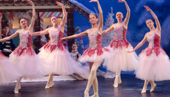 Ballerinas dancing on stage with The Nutcracker set in the background.