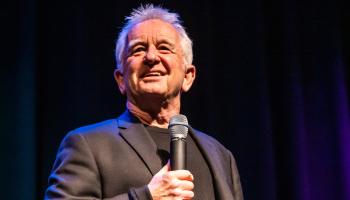 An image of Ron James on stage holding a microphone.