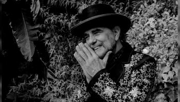 Daniel Lanois sits on a black and white soundstage.