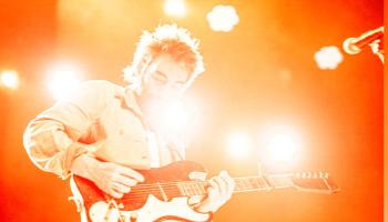 Leif stands on a smoky, colourful stage holding a guitar.