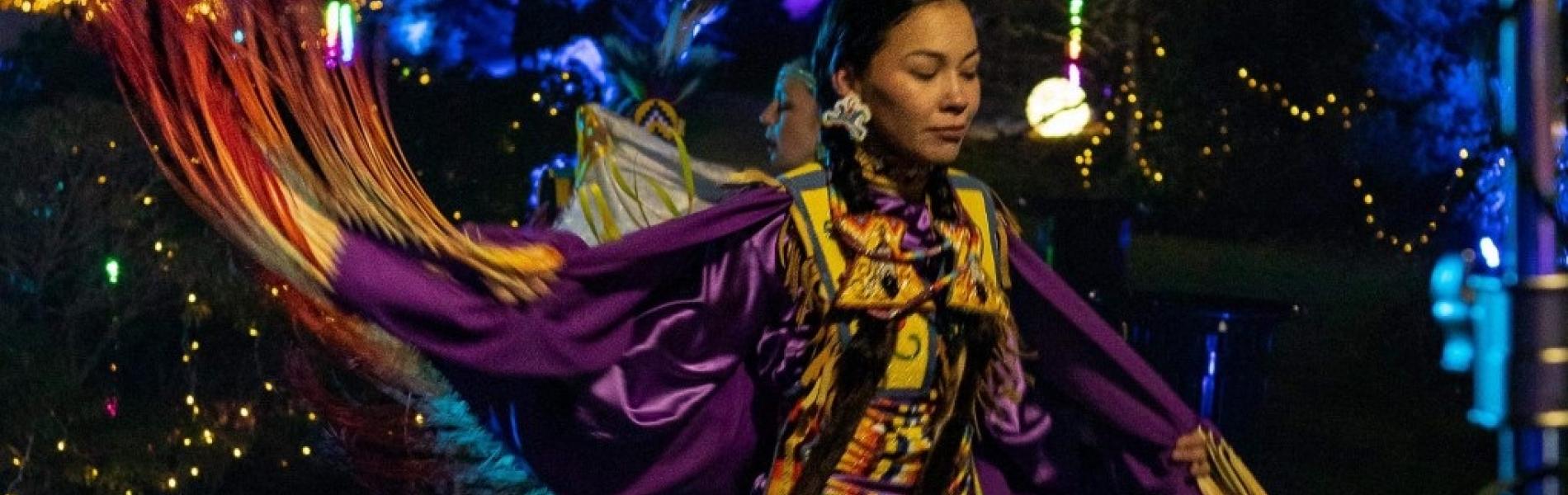 An Indigenous woman dancing dressed in traditional clothes.