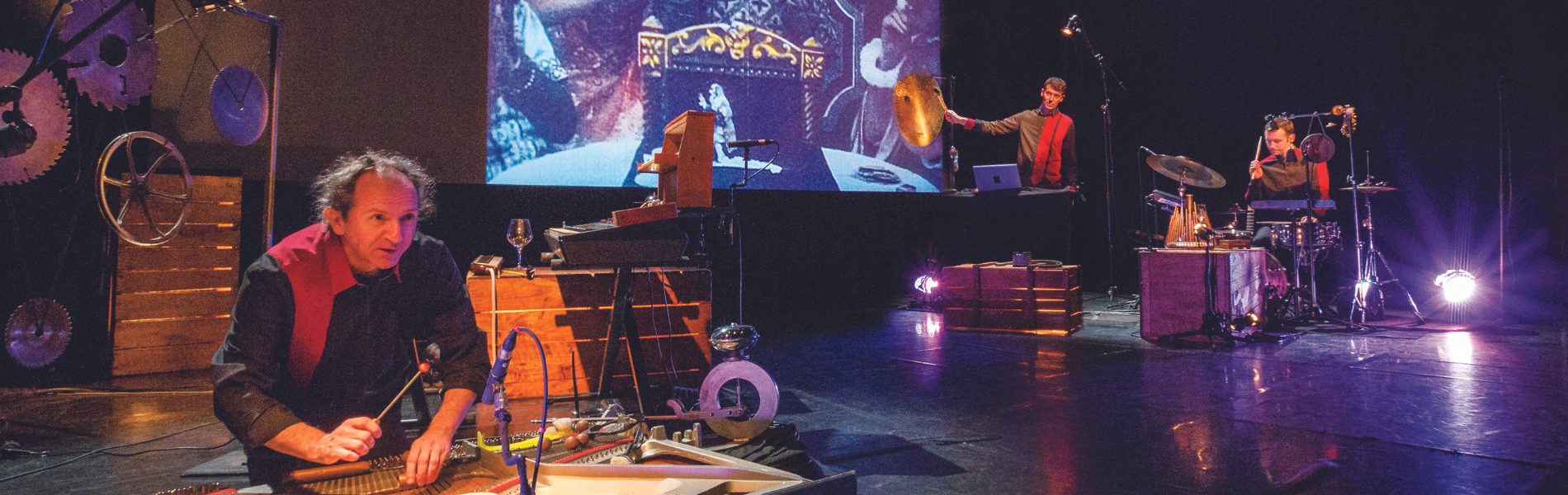 A photo of a stage filled with equipment to make different sounds and music while a film is projected in the background