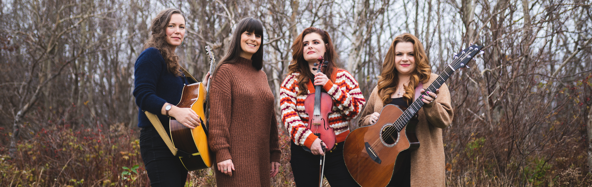 Four women holding instruments, standing together in front of bare trees