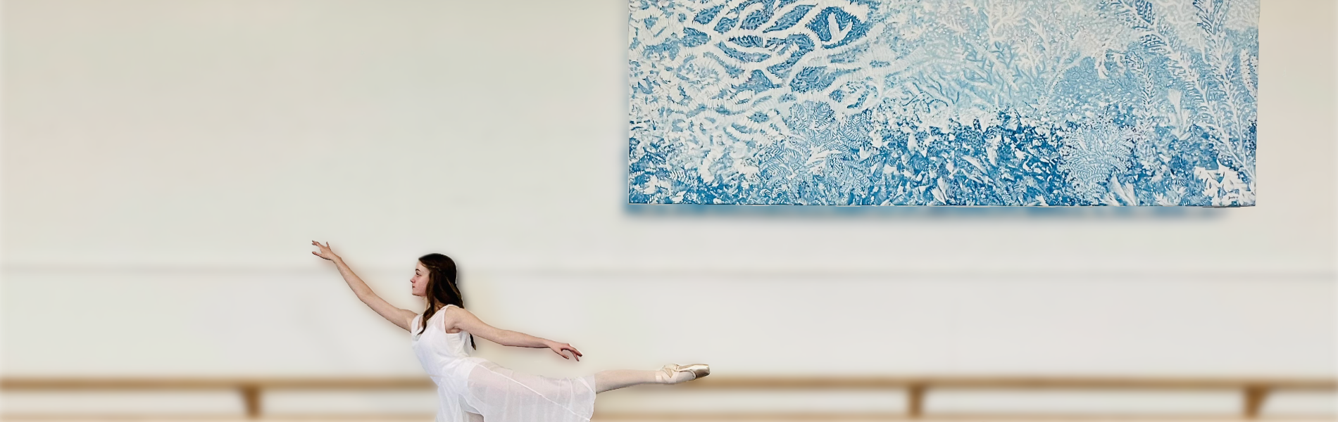 A young ballerina in white posing in front of a ballet barre.