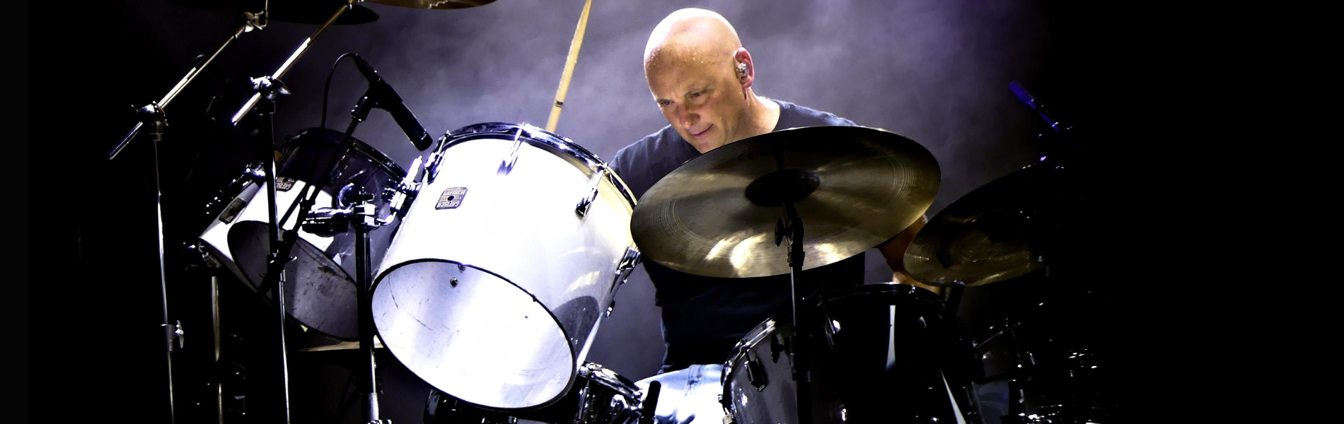 Martin Levac sitting at a bright white drum kit against a dark background