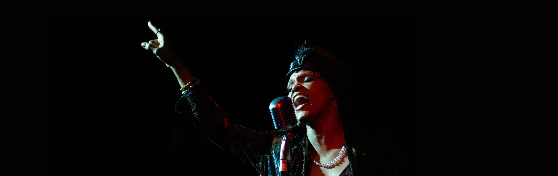 A close up, darkly lit image of a burlesque singer at an old fashioned microphone