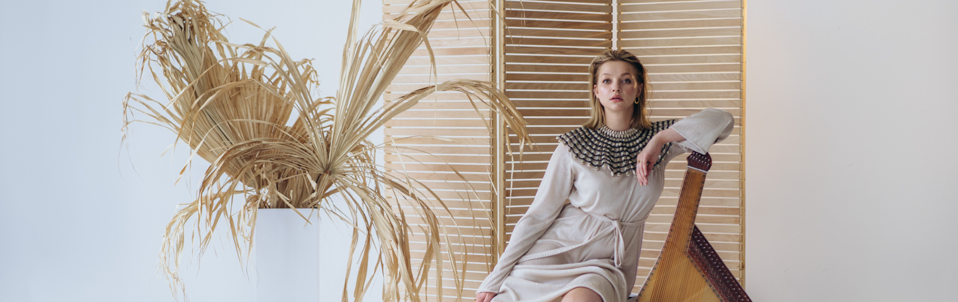 Maryna Krut sitting and leaning against the bandura with a tan background and plant next to her