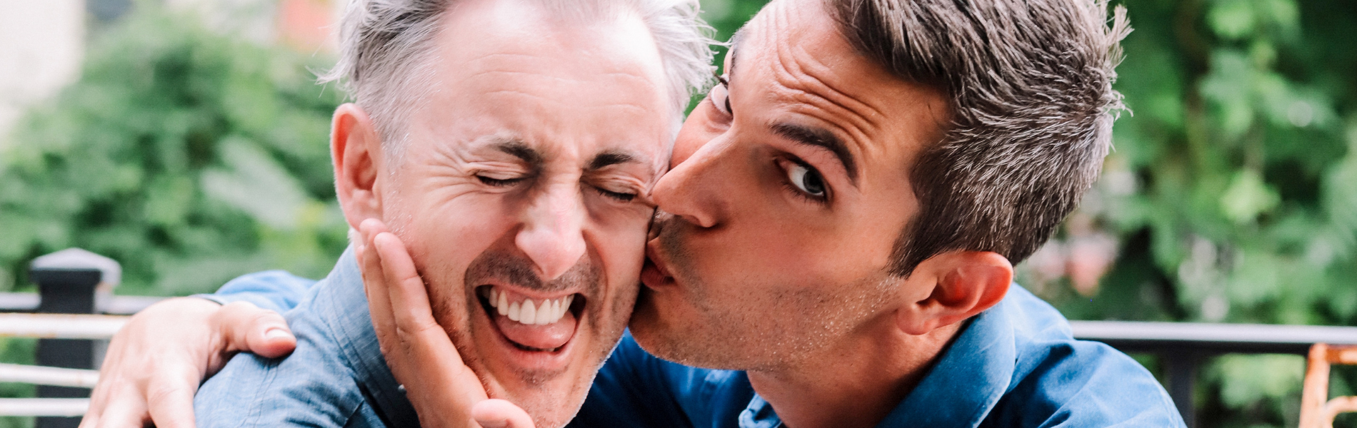 Alan Cumming making a scrunched face as Ari Shapiro kisses his cheek