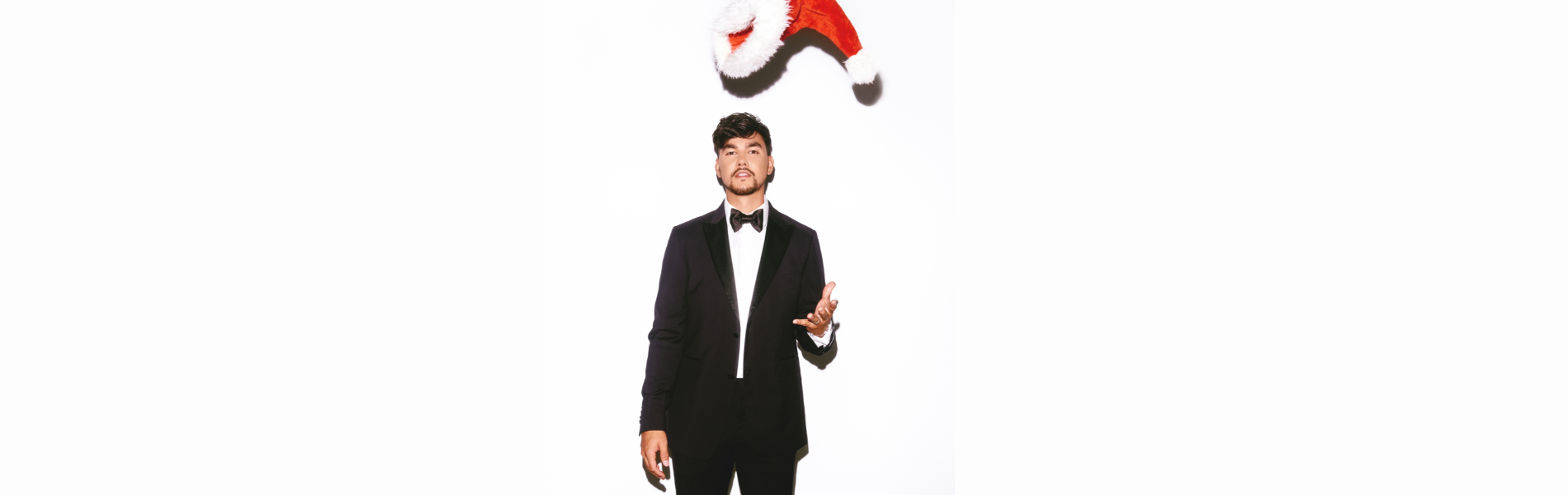 Tyler Shaw in a black suit tossing a Santa hat in the air, standing against a white background