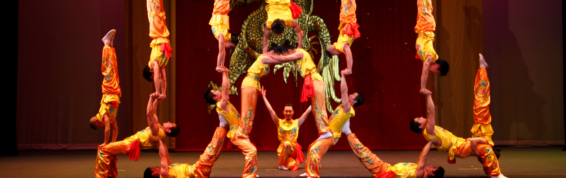 Performers with the Peking Acrobats in colourful yellow and red clothes posed together in a human pyramid shape