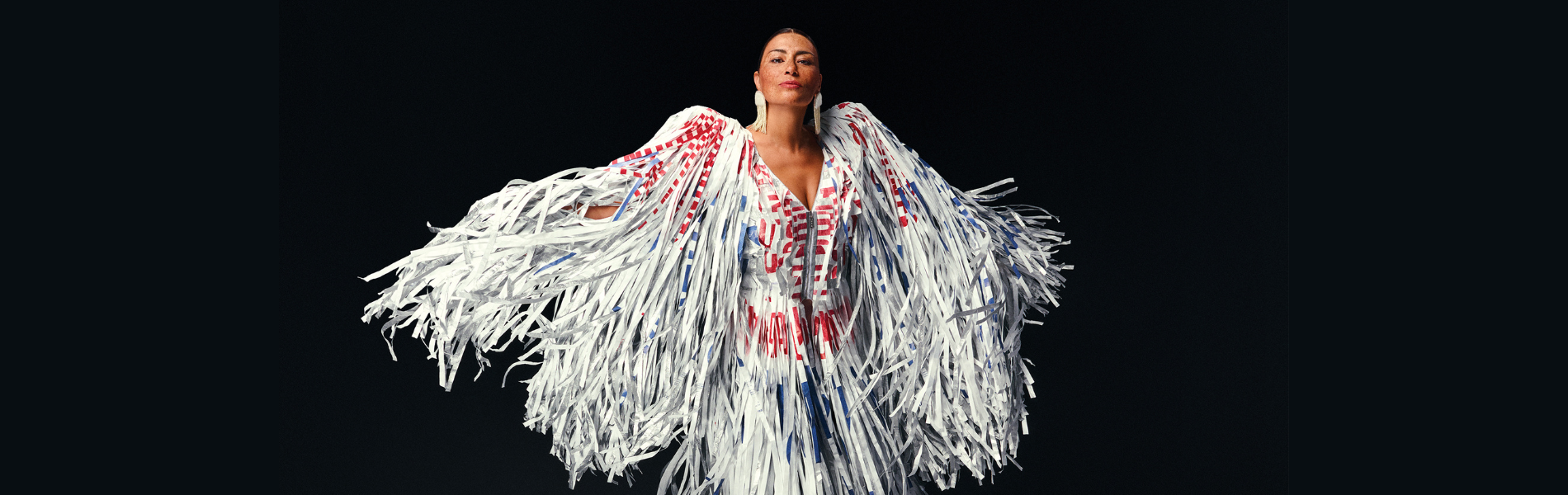 Elisapie in a white Indigenous ribbon dress, arms outstretched with the sleeves flowing around her