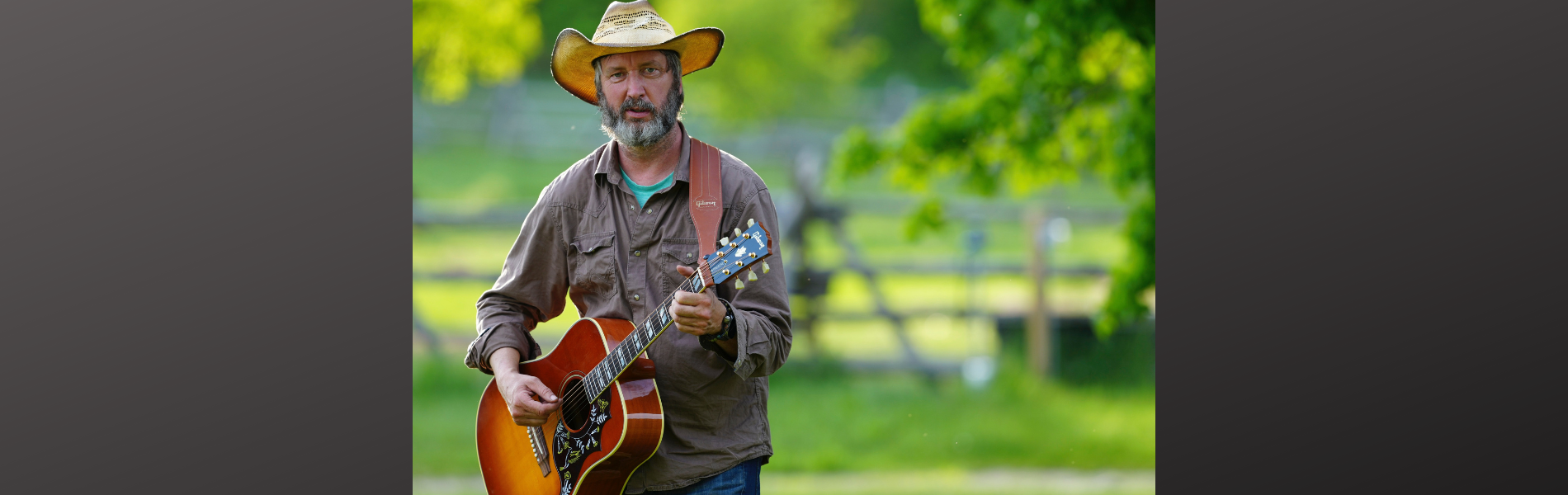 An image of Tom Green playing a guitar in a field of green.