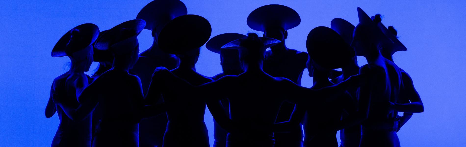 Dancers stand in shadows against a blue background.