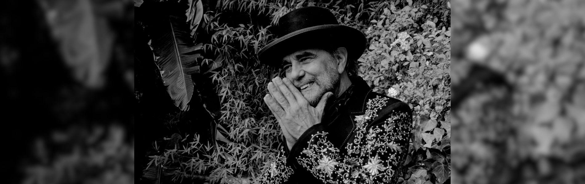 Daniel Lanois sits on a black and white soundstage.