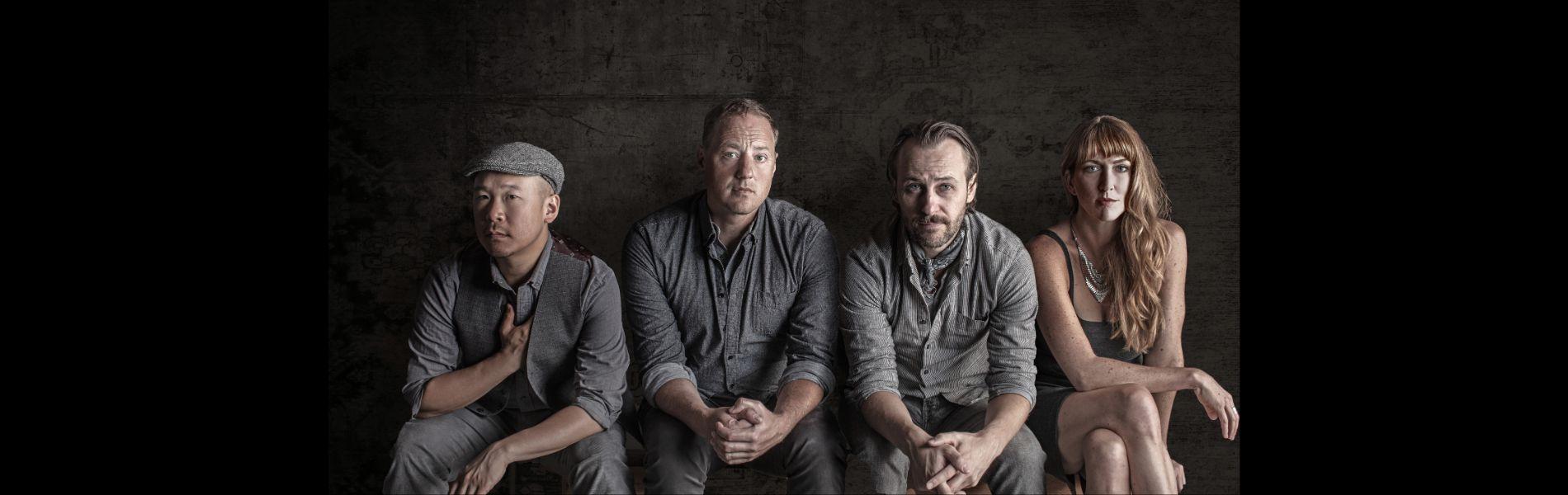 The four band members sit against a wooden wall.